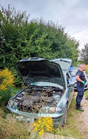 otwarta maska pojazdu bmw a obok niego stoi policjant