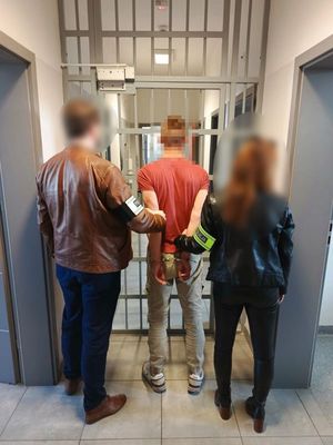 Policjanci wprowadzają zatrzymanego do pomieszczenia dla osób zatrzymanych.
