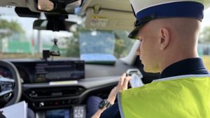 Policjant sierdzi w radiowozie i sprawdza coś na urządzeniu mobilnym