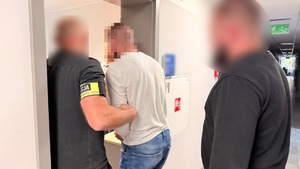 Policjanci wprowadzają zatrzymanego do pokoju służbowego.