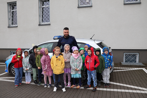 Policjant razem z dziećmi pozuje na tle radiowozu do grupowego zdjęcia