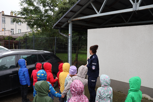 Policjantka opowiada dzieciom o policyjnym psie - dzieci stoją przy wybiegu dla policyjnych psów i przy płocie stoi pies.