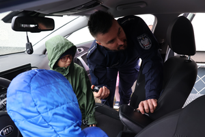 Dzieci siedzą w radiowozie a policjant pokazuje im radiostację