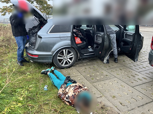Policjanci zatrzymali mężczyznę, leży w kajdankach na ziemi przy samochodzie.