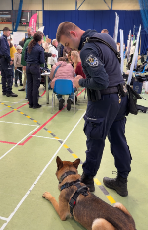 Policjant z psem służbowym w tle rozmowy pozostałych policjantów z uczestnikami targów
