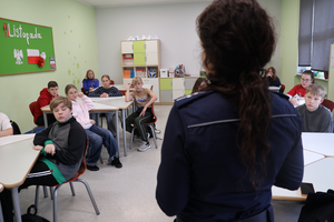 Policjantka prowadzi spotkanie, uczniowie siedzą w ławkach i słuchają.