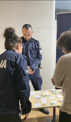 Policjanci rozmawiają z rodzicami i tłumaczą jak niebezpieczne są narkotyki i co przestawiają rekwizyty wystawione na stole.