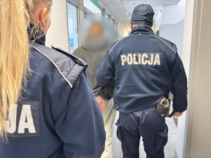 Policjanci prowadzą zatrzymanego nieletniego korytarzem komendy.
