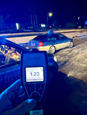 Zdjęcie wyniku badania alko - testem oraz w tle zatrzymany pojazd a także radiowóz