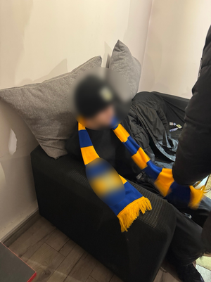 Chłopak siedzi na kanapie ubrany na sobie ma szalik w barwach żółto niebieskich - w szerokie pasy