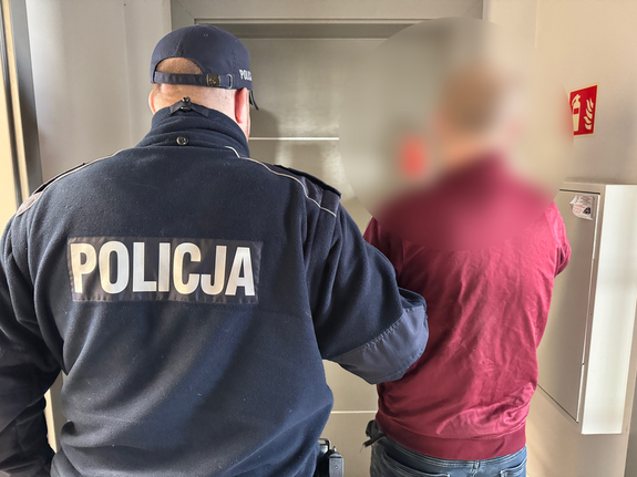 Mężczyzna jest prowadzony przez policjanta korytarzem komendy