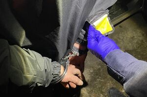 Policjant zakłada kajdanki mężczyźnie na ręce trzymane z tyłu.