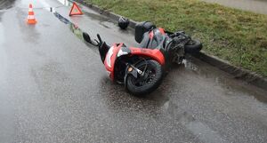 Dwa pojazdy uczestniczące w zdarzeniu, skuter leżący na drodze oraz czarna skoda