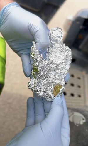 Policjant otwiera zawiniątko w którym znajduje się zielona kulka suszu - który wyglądem przypomina marihuanę