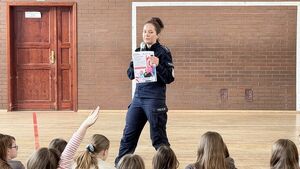 Policjantka prowadzi spotkanie na sali gimnastycznej, dzieci siedzą i słuchają.