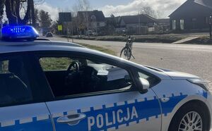 Policyjny radiowóz przy drodze, w tle rower i samochód osobowy