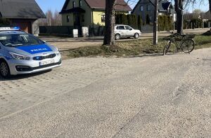 Policyjny radiowóz przy drodze, w tle rower i samochód osobowy