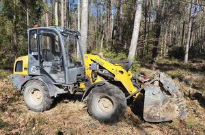 W lesie stoi ładowarka w kolorze żółto szarym