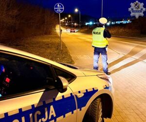 Policjant stoi nocą przy drodze i mierzy prędkość oddalających się samochodów