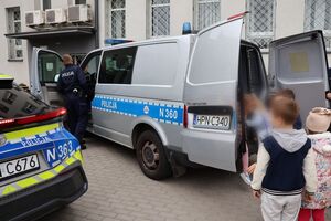 Policjanci oprowadzają dzieci po dziedzińcu komendy, pokazują radiowozy oraz prowadzą spotkanie na sali odpraw, podczas którego dzieci korzystają z zabawek edukacyjnych (samochodów i drogi z przejściem dla pieszych)