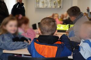 Policjanci oprowadzają dzieci po dziedzińcu komendy, pokazują radiowozy oraz prowadzą spotkanie na sali odpraw, podczas którego dzieci korzystają z zabawek edukacyjnych (samochodów i drogi z przejściem dla pieszych)