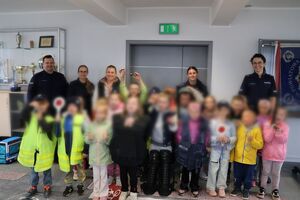 Policjanci oprowadzają dzieci po dziedzińcu komendy, pokazują radiowozy oraz prowadzą spotkanie na sali odpraw, podczas którego dzieci korzystają z zabawek edukacyjnych (samochodów i drogi z przejściem dla pieszych)