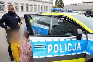 Policjanci oprowadzają dzieci po dziedzińcu komendy, pokazują radiowozy oraz prowadzą spotkanie na sali odpraw, podczas którego dzieci korzystają z zabawek edukacyjnych (samochodów i drogi z przejściem dla pieszych)