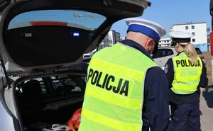 Zdjęcie policjantów przy radiowozie oraz samochodu mercedes, który rozbił się uderzając w dom jednorodzinny.