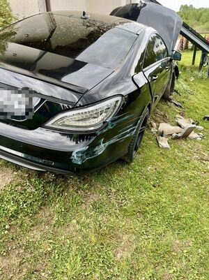 Zdjęcie policjantów przy radiowozie oraz samochodu mercedes, który rozbił się uderzając w dom jednorodzinny.