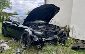 Zdjęcie policjantów przy radiowozie oraz samochodu mercedes, który rozbił się uderzając w dom jednorodzinny.