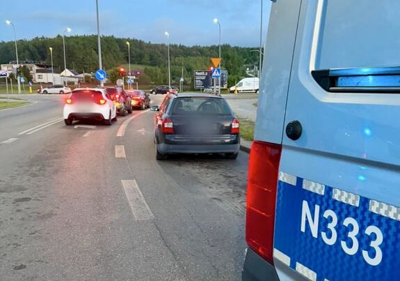 Policjanci stoją radiowozami na ulicy a przy nich stoi zatrzymywany samochód osobowy.
