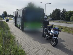 Przy autokarze stoi policjant oraz jego służbowy motocykl