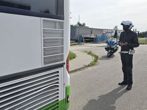 Przy autokarze stoi policjant oraz jego służbowy motocykl