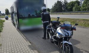 Przy autokarze stoi policjant oraz jego służbowy motocykl