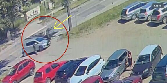 NA zdjęciu widoczny jest jasny samochód który skręca w lewo wjeżdżając na duży parking, a na kolejnym radiowóz i karetkę widać także oraz inne osoby, będące w koło.