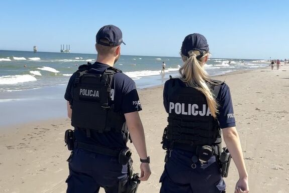 Policjanci ci w patrolu pieszym idą brzegiem morza