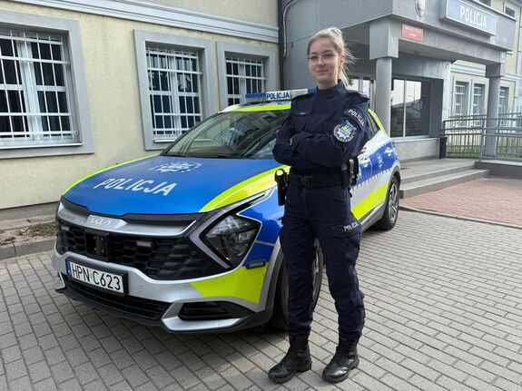 Policjantka stoi przy radiowozie z założonymi rękoma.