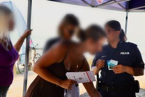 Policjantka rozmawia z turystami, rozdaje opaski niezgubki i obserwuje jak turyści pokonują tor przeszkód w alko-googlach.