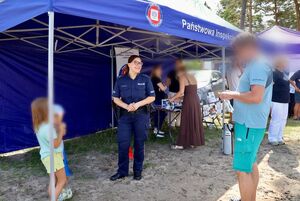 Policjantka rozmawia z turystami, rozdaje opaski niezgubki i obserwuje jak turyści pokonują tor przeszkód w alko-googlach.