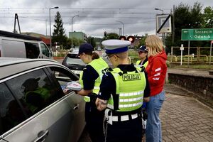 Policjanci ze strażnikami ochrony kolei rozmawiają z kierowcami, którzy zatrzymali się przed przejazdem kolejowym na zamkniętych rogatkach.