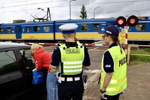 Policjanci ze strażnikami ochrony kolei rozmawiają z kierowcami, którzy zatrzymali się przed przejazdem kolejowym na zamkniętych rogatkach.