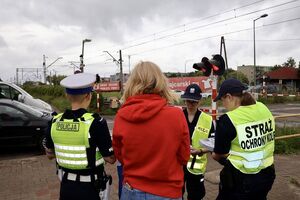 Policjanci ze strażnikami ochrony kolei rozmawiają z kierowcami, którzy zatrzymali się przed przejazdem kolejowym na zamkniętych rogatkach.