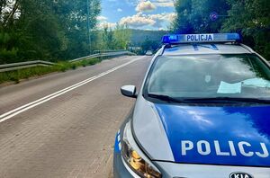 Policjanci pracują na miejscu wypadków, na zdjęciu widoczny jest niebieski samochód z rozbitym przodem, motocykl, rowerzysta przejeżdżający przed maską samochodu oraz radiowóz postawiony za białym samochodem oraz w innym miejscu radiowóz stojący przy chodniku.