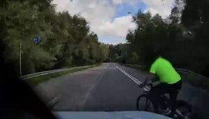 Policjanci pracują na miejscu wypadków, na zdjęciu widoczny jest niebieski samochód z rozbitym przodem, motocykl, rowerzysta przejeżdżający przed maską samochodu oraz radiowóz postawiony za białym samochodem oraz w innym miejscu radiowóz stojący przy chodniku.