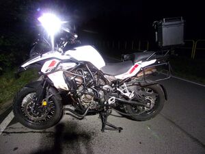 Policjanci pracują na miejscu wypadków, na zdjęciu widoczny jest niebieski samochód z rozbitym przodem, motocykl, rowerzysta przejeżdżający przed maską samochodu oraz radiowóz postawiony za białym samochodem oraz w innym miejscu radiowóz stojący przy chodniku.