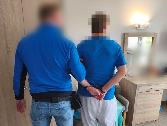 Policjant trzyma zatrzymanego, który trzyma ręce z tyłu w kajdankach.