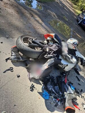 Roztrzaskany motocykl leży na jezdni i obok niego buty motocyklowe i kask położony na motocyklu