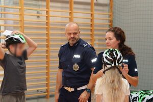 Policjanci prowadzą spotkanie z dziećmi -w tle na stołach widoczne są kaski dla uczniów